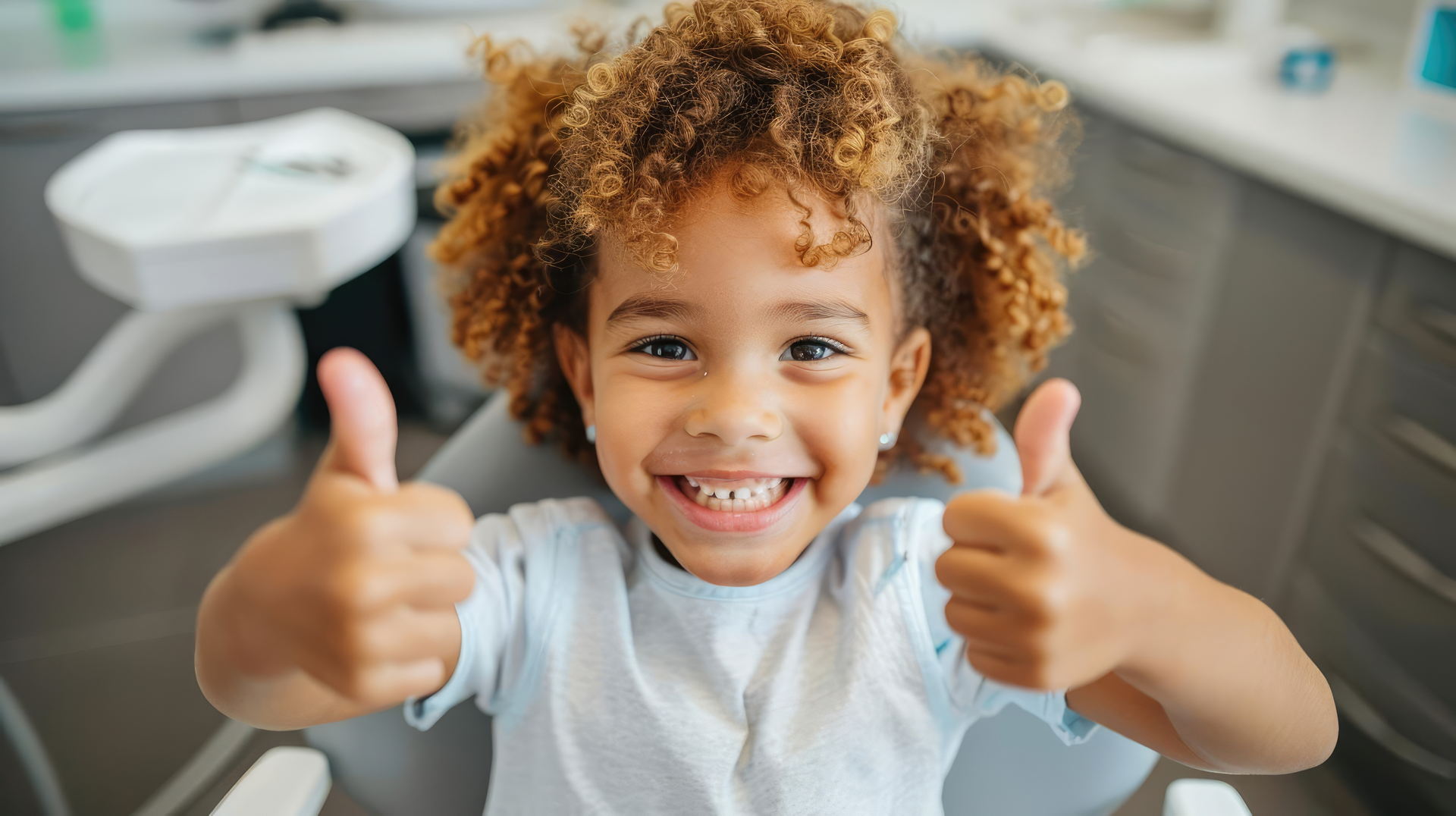 Happy child giving thumbs up in dentist chair, positive dental checkup a girl with curly hair giving thumbs up
