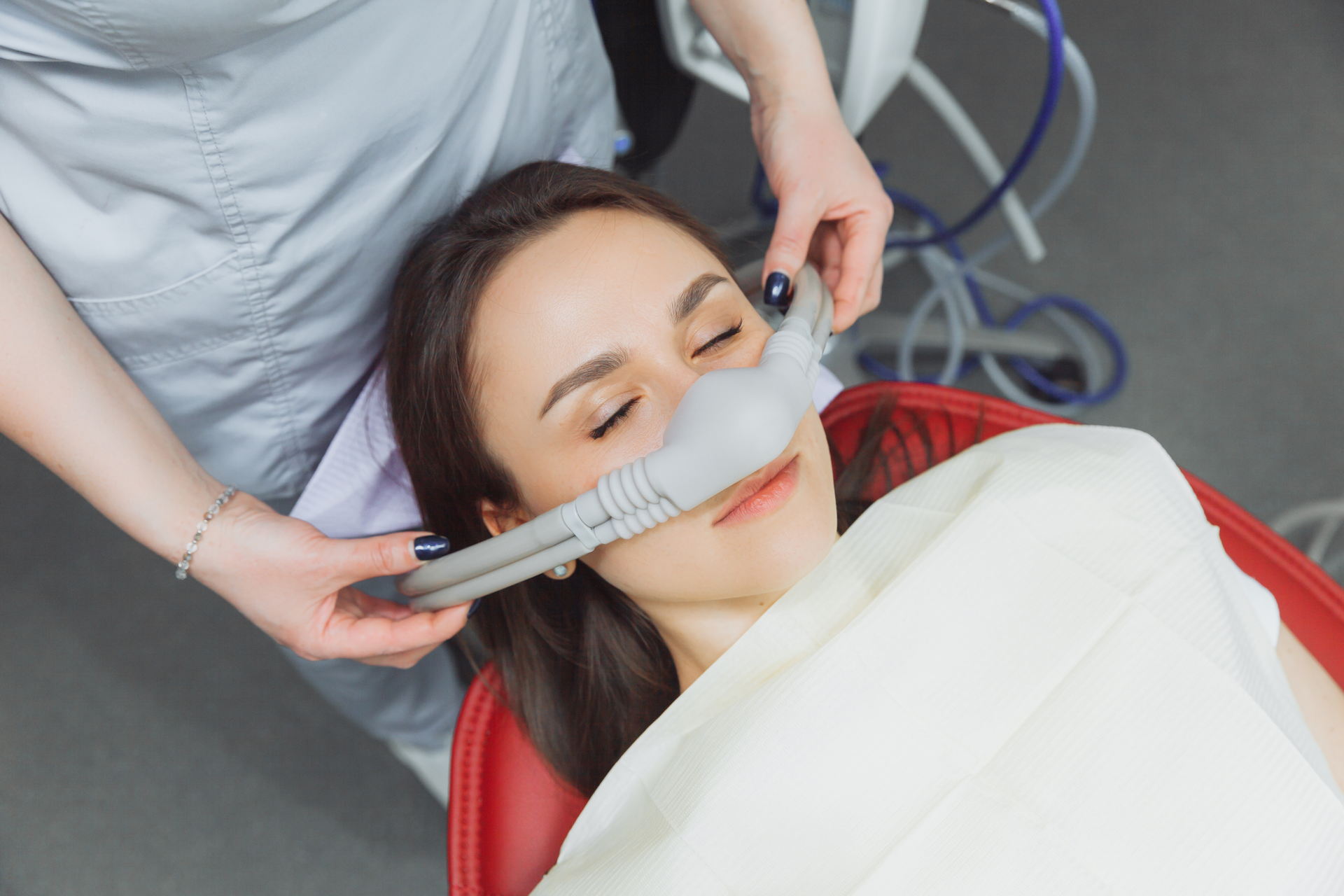 dentist puts inhalation sedative mask on his patient. a woman lying down with a tube attached to her face